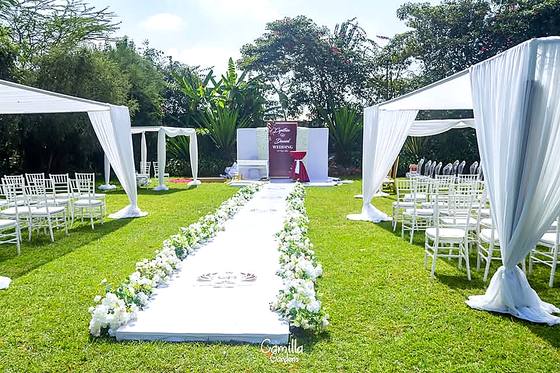 Two white draped pergolas either side of a white aisle runner lined with petals, leading to an altar table