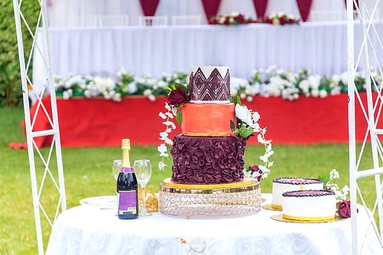 Tiered burgundy and gold wedding cake on the top table with a red backdrop behind