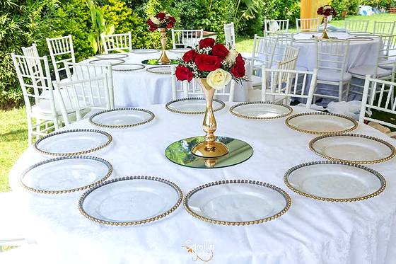 Round reception tables laid with gold charger plates and tall red rose centrepieces