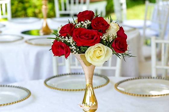 Red and white rose centrepiece in a tall gold vase on a laid reception table