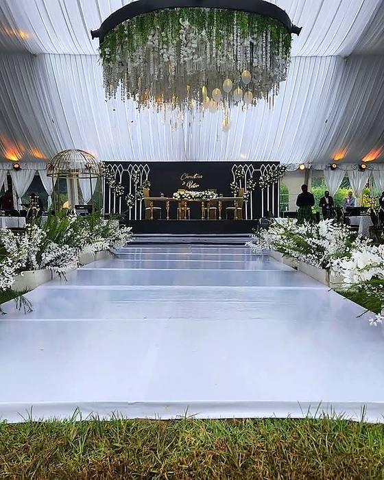 Large floral chandelier suspended above a white aisle inside a dark-draped marquee