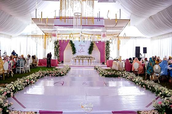 Guests seated inside a draped marquee facing a white aisle lined with pink and white flowers