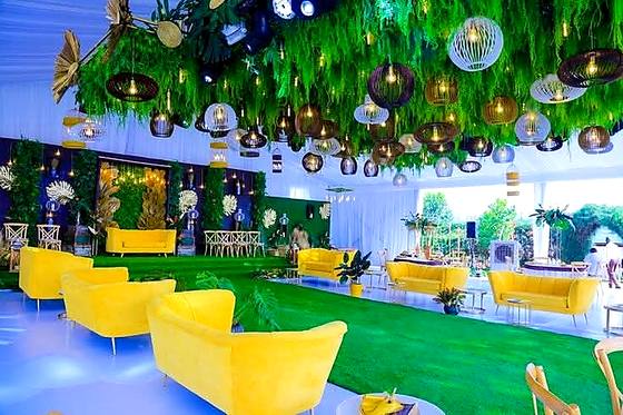 Yellow lounge sofas on green carpet beneath a ceiling of hanging foliage and glass globes
