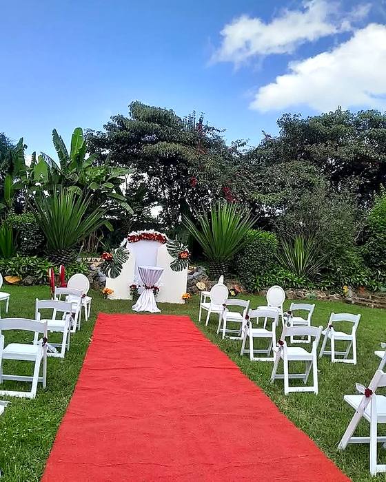 Red carpet aisle between rows of white chairs leading to a draped altar table under a blue sky