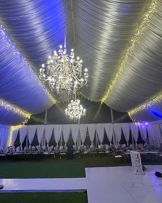 Crystal chandelier and fairy lights hung under marquee draping lit in blue and violet