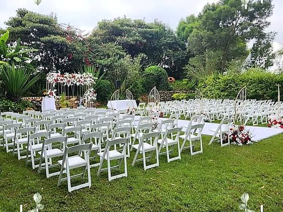 Rows of white folding chairs facing a white-and-red floral arch on the church grounds