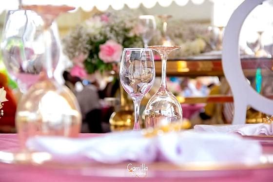 Gold-rimmed wine glasses and a pink and white floral centrepiece on a dressed reception table