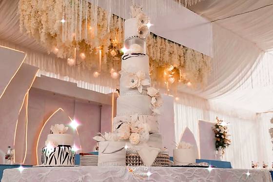 White and gold tiered wedding cake on a table beneath a draped ceiling hung with flowers