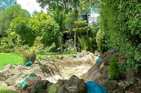 Rockery at Camilla Gardens built from pale boulders with shrubs and a water feature set into the lawn