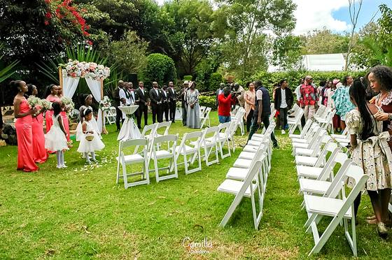 Guests in bright dress standing at their seats as the bridal party walks down the aisle on the lawn