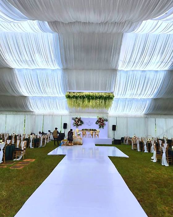 Tiered white draping across the marquee ceiling above a white aisle with guests seated either side