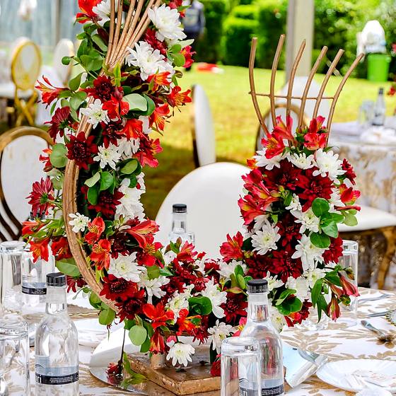 Tall red rose arrangement with gold detailing on a reception table beside a white chair