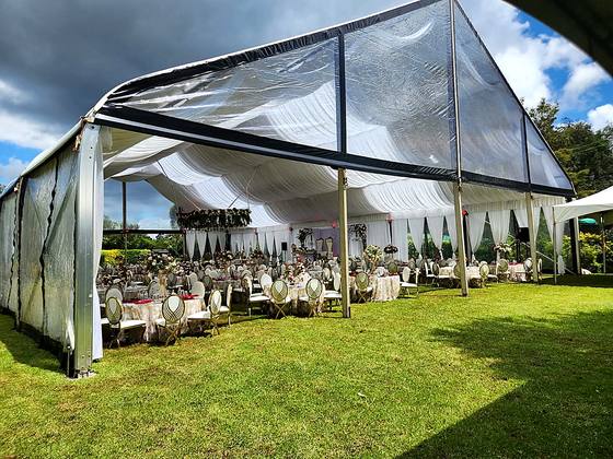Clear-roofed marquee open to the lawn with tables set beneath and garden trees behind