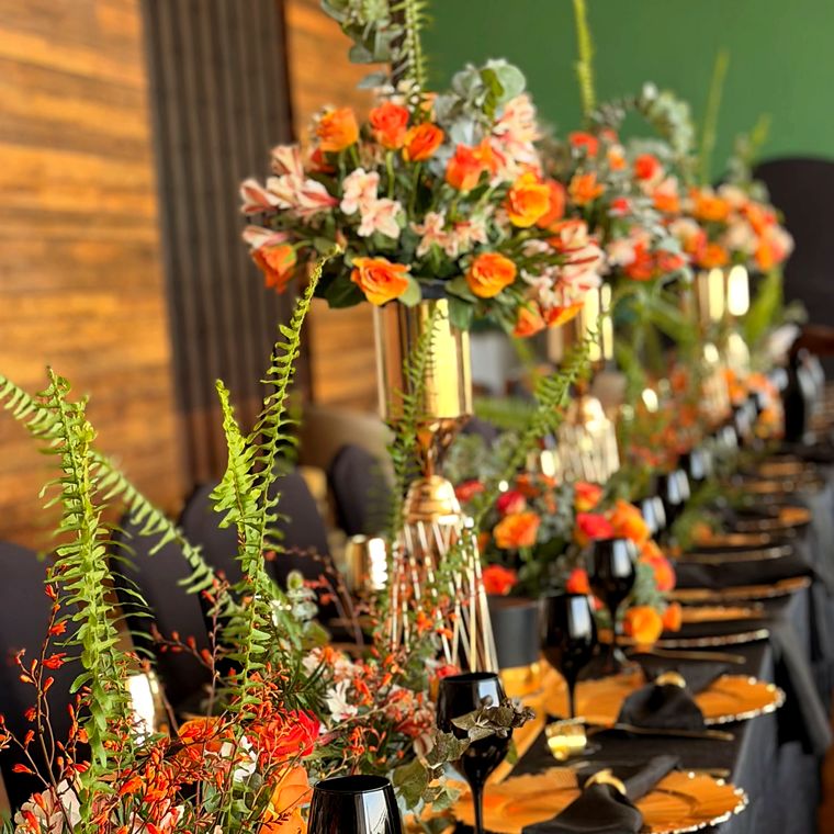 Orange rose and fern centrepieces on tall gold stands over black glassware