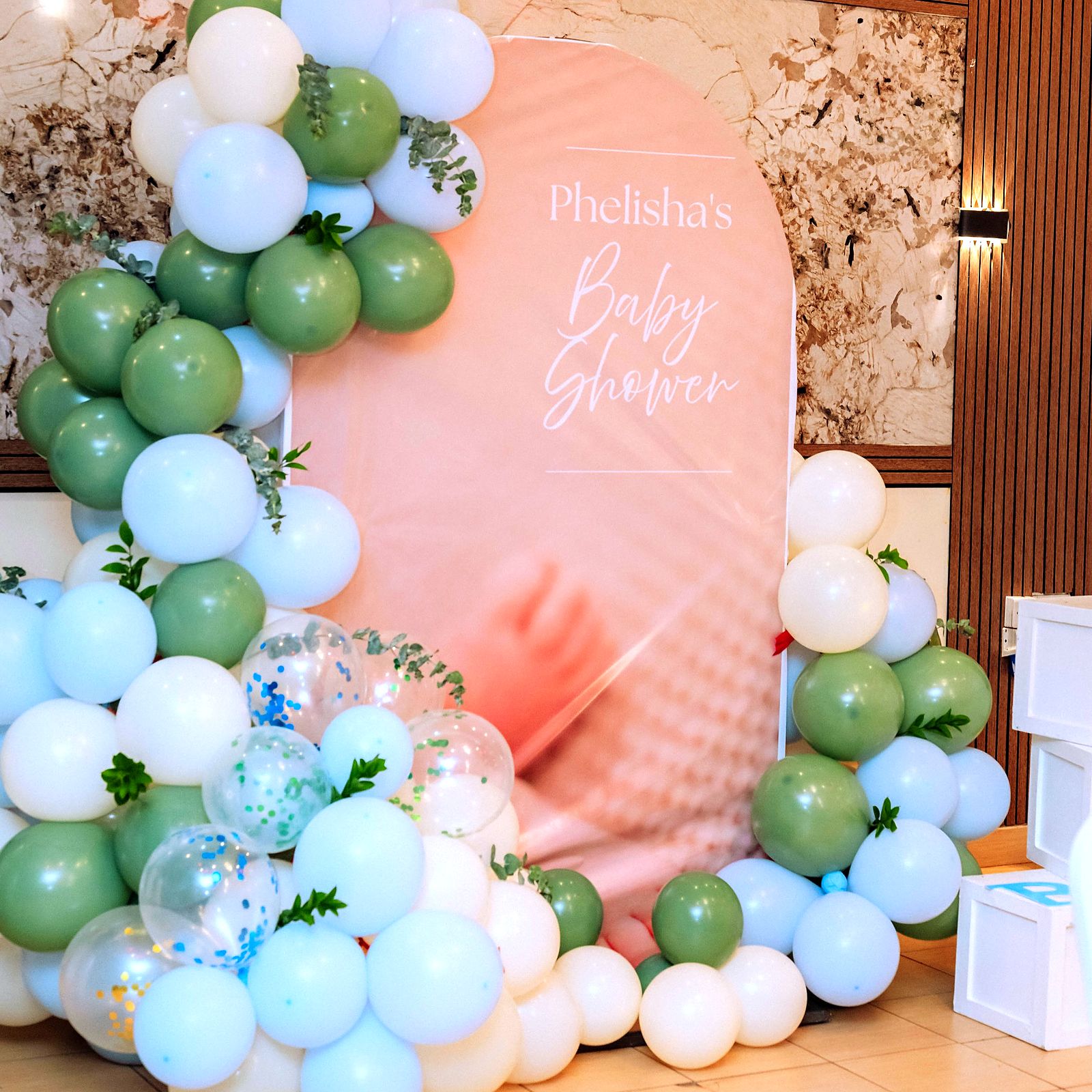 Baby shower backdrop framed by a sage, white and powder-blue balloon garland