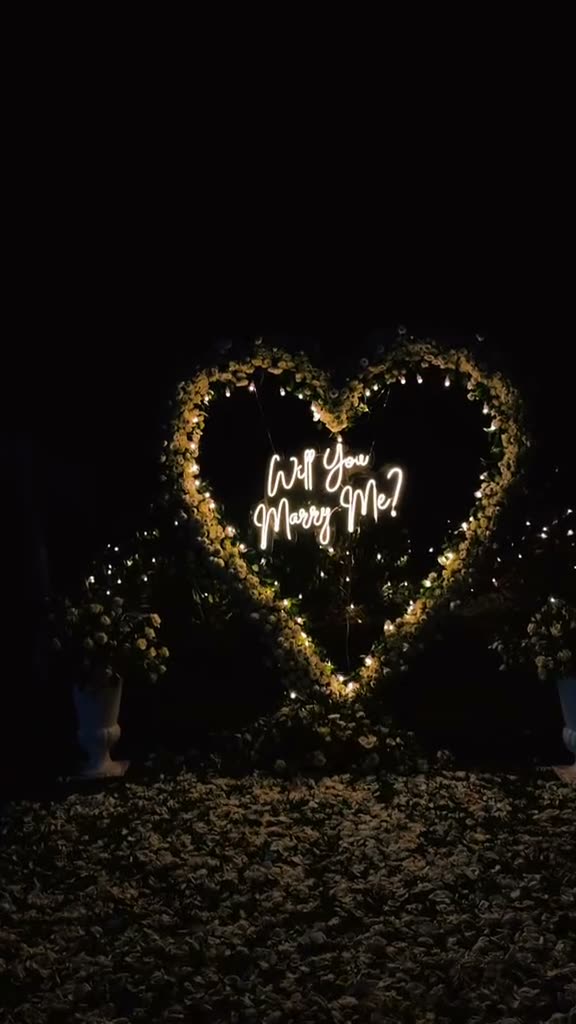 A glowing fairy-light heart reading Will you marry me at night, with lanterns and petals