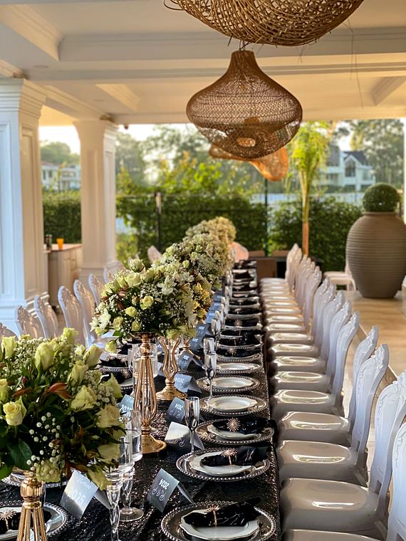 Long veranda dinner table with white roses on gold stands and silver beaded chargers