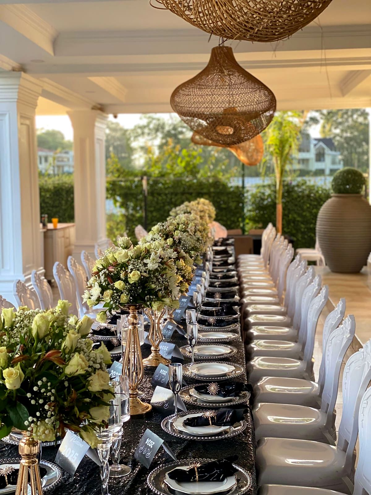 Long veranda dinner table with white roses on gold stands and silver beaded chargers