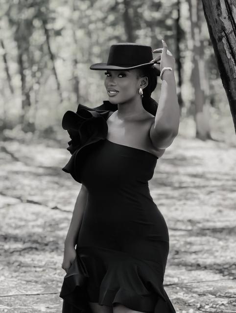 Black-and-white portrait of a woman tipping a flat-brim hat in a forest