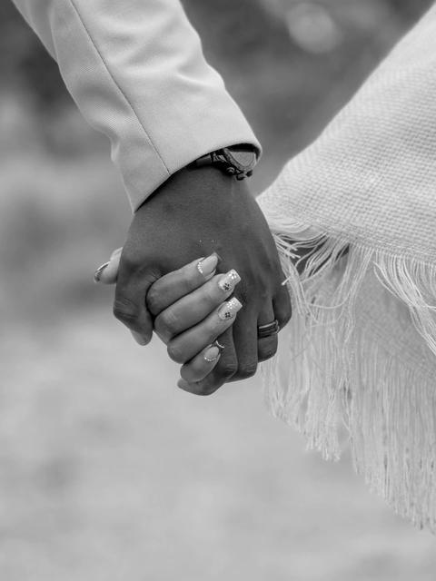 Black-and-white close-up of a couple holding hands, engagement ring visible