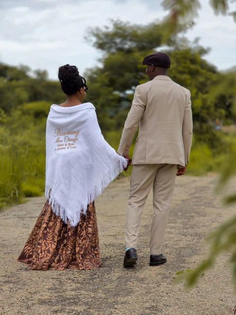 Couple walking away hand in hand along a country road, her shawl embroidered with their names