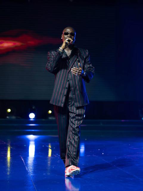Fireboy DML walking across a blue-lit stage in a pinstripe suit, singing into a microphone