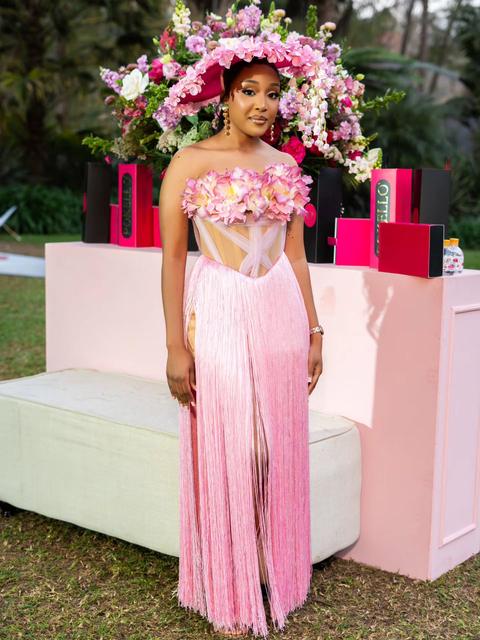 Full-length portrait of a woman in a pink fringed floral gown and hat beside a pink event display