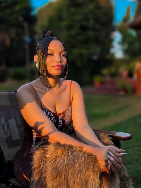 Woman in a corset top seated on a fur throw on a garden chair at golden hour