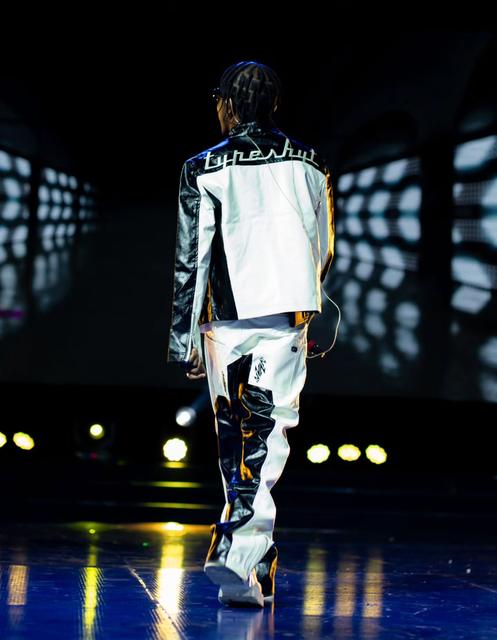 Nutty O walking away from the camera on stage, his name across the back of his jacket, lights reflecting off the floor