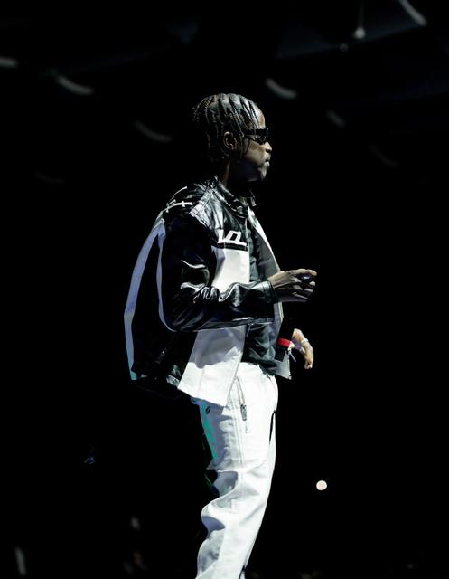 Nutty O on a dark stage in a black-and-white leather jacket and white trousers