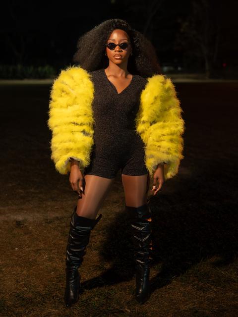 Full-length night portrait of a woman in yellow feather sleeves, black playsuit and thigh-high boots